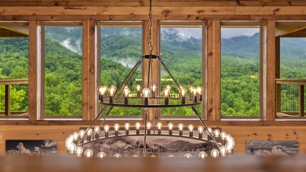 Una habitación con una lámpara circular, ventanas amplias que dan a vistas de montañas y paredes de madera.