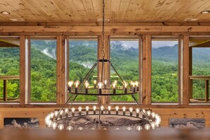 Ein Zimmer mit einem runden Kronleuchter, großen Fenstern mit Blick auf Berge und Holzwänden.