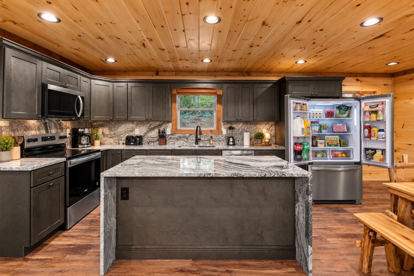 A modern kitchen with dark cabinetry, a marble island, and a built-in refrigerator.