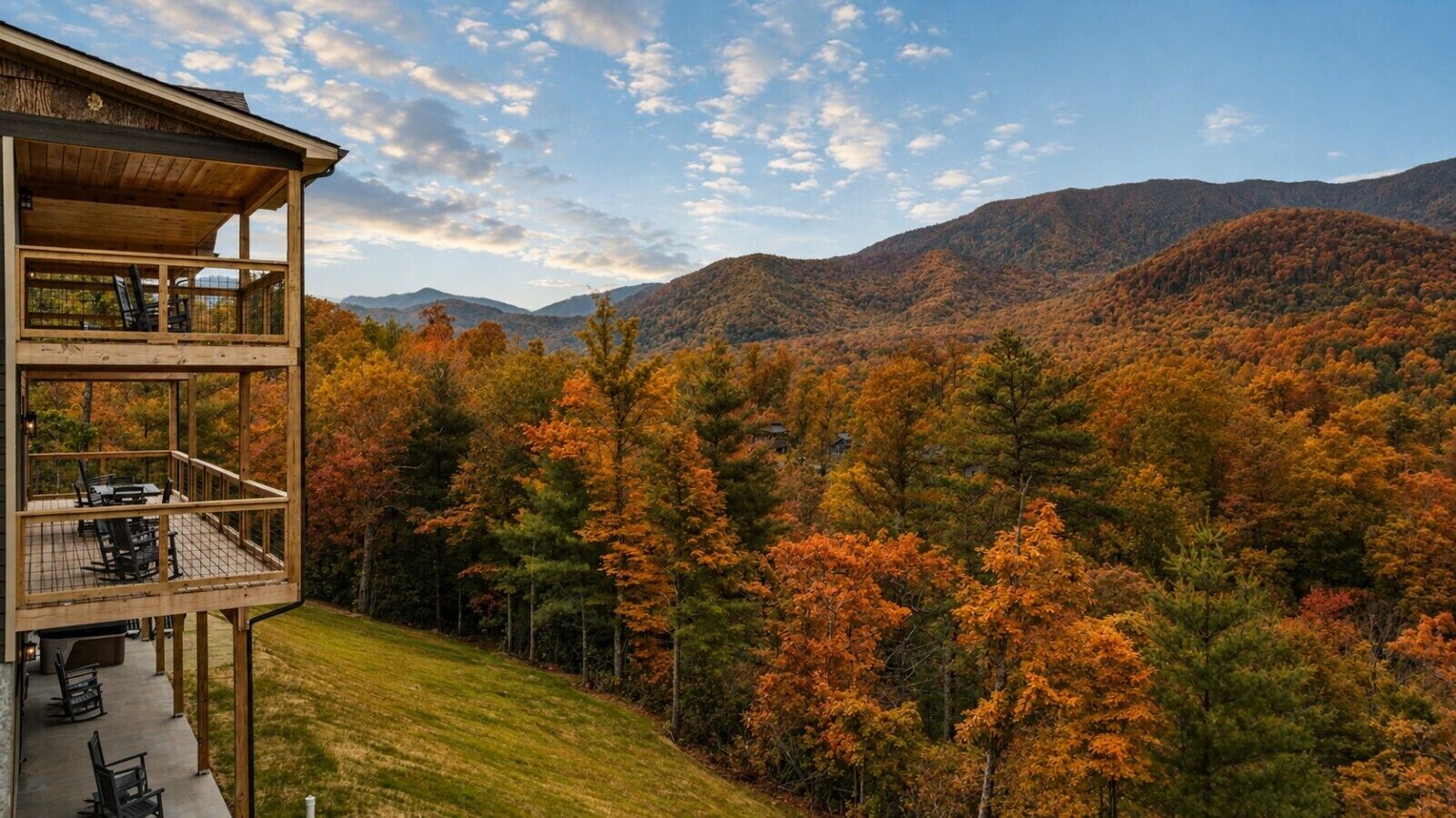 A multi-level wooden cabin with a deck, overlooking a forested mountain range.