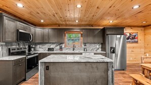 Una cocina moderna con encimeras de granito, electrodomésticos de acero inoxidable y techo de madera.