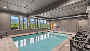 An indoor swimming pool with a view of greenery outside, a lifeguard chair, and a door with a sign.