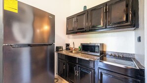 A kitchen with a stainless steel refrigerator, a microwave, a stove, and black cabinets. - Central One Bedroom Apartment on Third Floor (Sosúa)