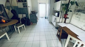En smal hall med en matplats på ena sidan, ett litet kök på den andra och en dörr som leder in till ett ljust rum.