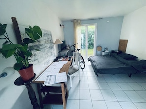 A room with a bed, a desk with papers, a bicycle, and a potted plant.
