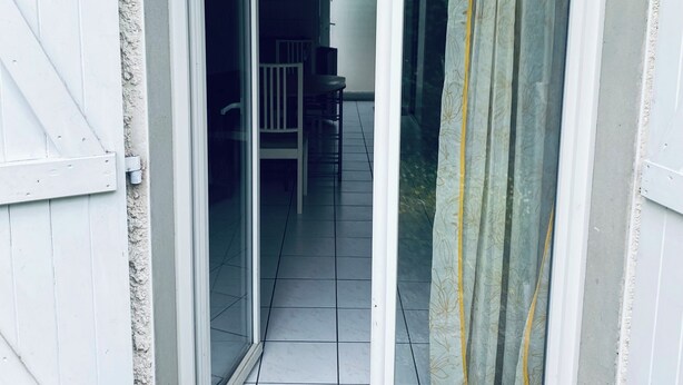 En dörröppning som leder ut till en balkong med en stol och ett bord, en vit dörr och en gardin.