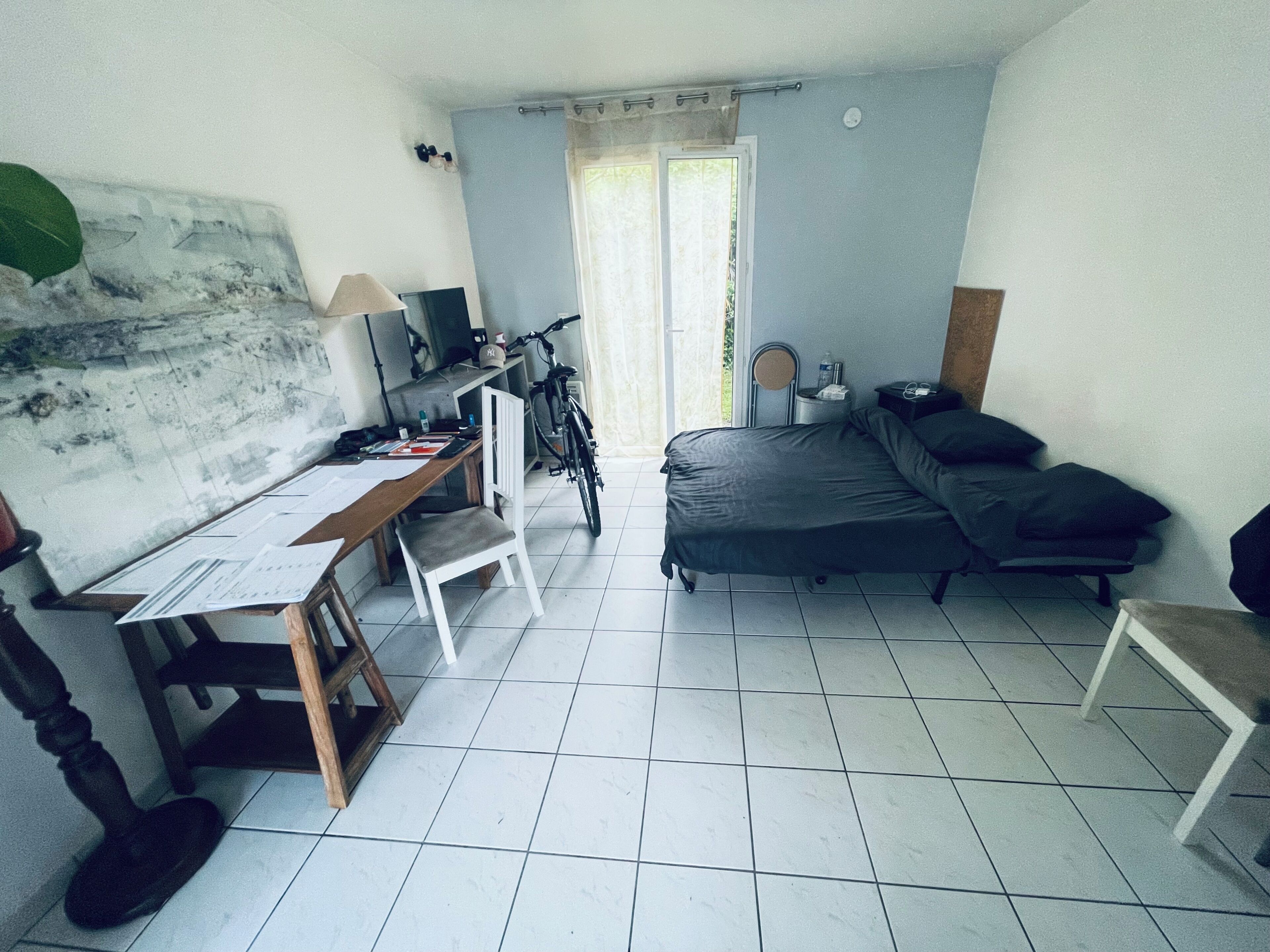 A compact room with a bed, desk, chair, bicycle, and a window.