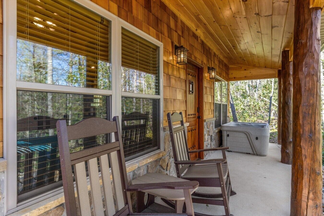 Eine Holzveranda mit zwei Schaukelstühlen, einem Whirlpool und großen Fenstern mit Blick auf einen Wald.