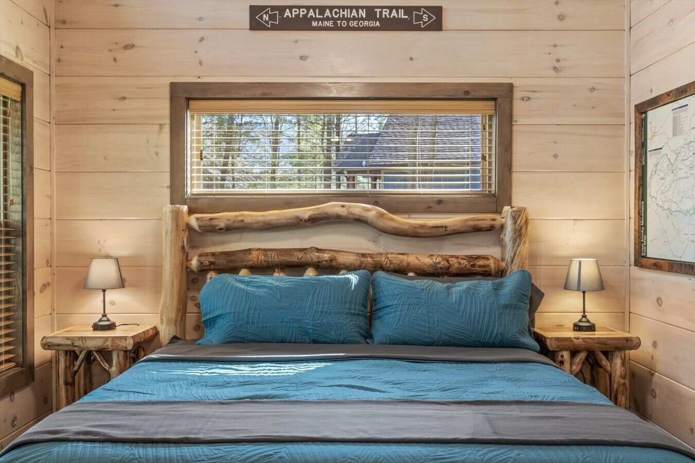 A wooden cabin room with a bed, two nightstands, a window, and a sign indicating the Appalachian Trail.