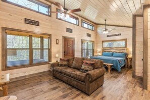 Eine Holzhütte mit Holzvertäfelung, einem Bett mit blauer Bettwäsche, einem braunen Ledersofa und einem Deckenventilator.