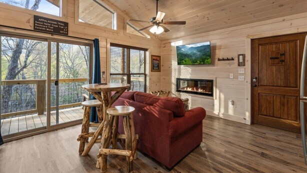 A cabin interior with a wooden floor, a red sofa, a fireplace, a television, and a sign indicating the Appalachian Trail. - Gatlinburg 23 min + Hot Tub + Fire Pit #1 (Cosby)