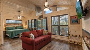 A cabin interior with a bed, a red sofa, a dining table, and a TV mounted on the wall. - Gatlinburg 23 min + Hot Tub + Fire Pit #1 (Cosby)