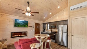 A cozy cabin interior with a fireplace, wooden walls, a kitchen with modern appliances, and a ceiling fan. - Gatlinburg 23 min + Hot Tub + Fire Pit #1 (Cosby)