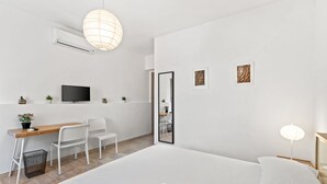 A bedroom with a bed, a desk with chairs, a TV, and artwork on the walls. - Camera chiara 3 – Relax with a View in the Heart of Alghero 🌊✨ (Alghero)