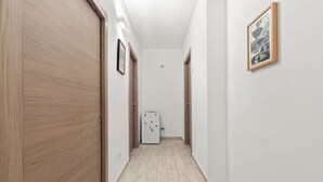 A narrow hallway with wooden doors, a refrigerator, and a framed picture on the wall. - Camera chiara 3 – Relax with a View in the Heart of Alghero 🌊✨ (Alghero)