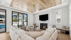 A modern living room with a large sectional sofa, a fireplace, a flat-screen TV, and a ceiling fan. - Retreat with Pool, LSV, Peloton and More (Santa Rosa Beach)