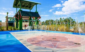 Ein Basketballplatz mit Wasserspielfeature, umgeben von einem Zaun und Palmen.