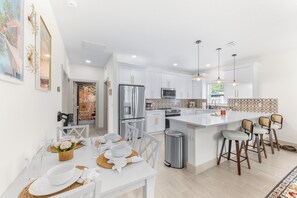A modern kitchen with white cabinetry, stainless steel appliances, and a central island with bar stools. - St Augustine Nights of Lights Near Downtown (St. Augustine)