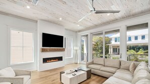 A modern living room with a fireplace, large windows, and a sectional sofa. - Gulf Views with LSV, Pool, Peloton & More (Santa Rosa Beach)