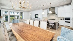 A spacious kitchen with white cabinets, a wooden dining table, and a chandelier. - Gulf Views with LSV, Pool, Peloton & More (Santa Rosa Beach)