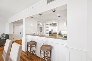 Una cocina moderna con armarios blancos, un refrigerador de acero inoxidable y una barra con taburetes.