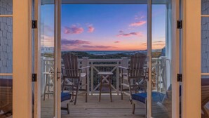 A balcony with a view of a sunset, two Adirondack chairs, and a small table. - Gulf View Condo with Community Amenities (Watersound)