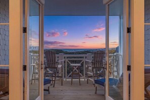 Un balcón con vista a un atardecer, dos sillas Adirondack y una mesa pequeña.