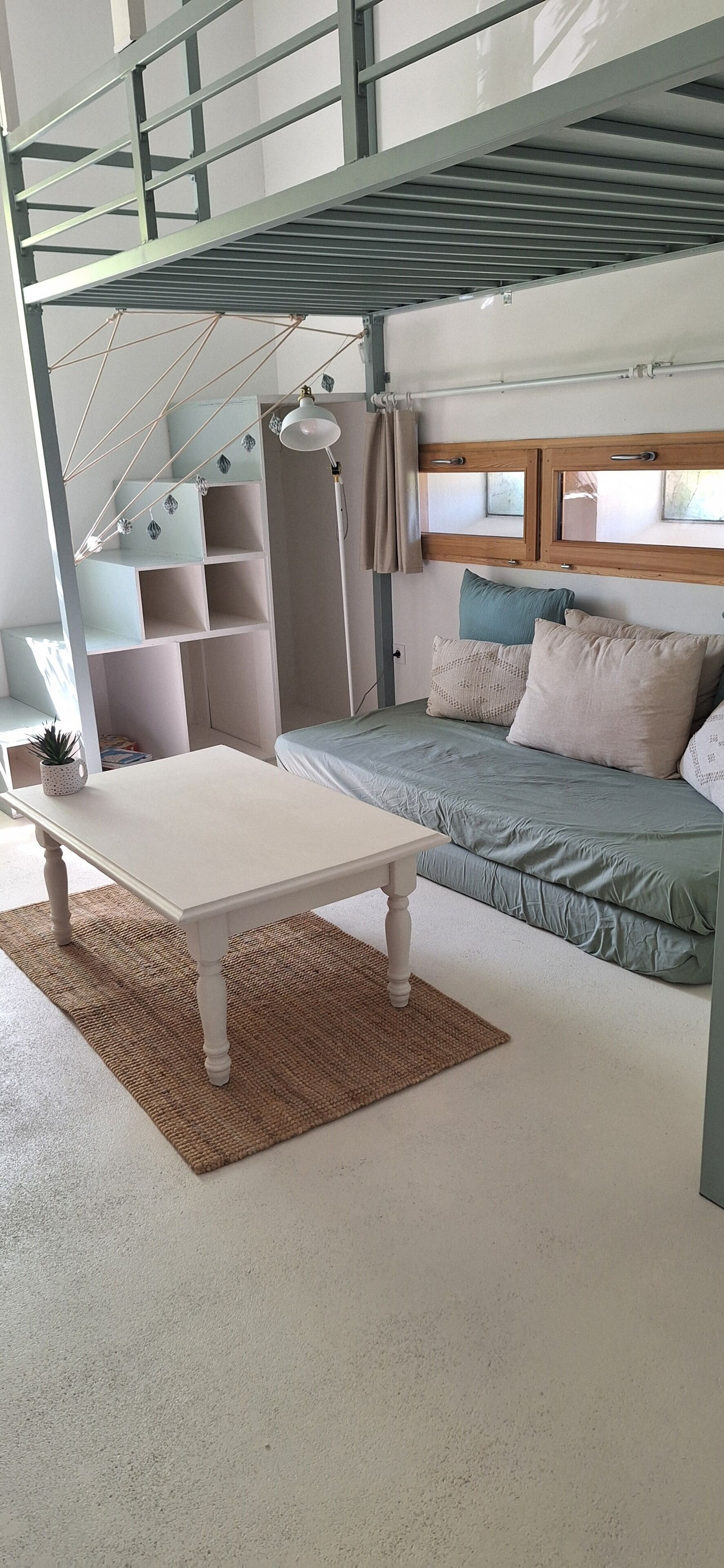 Een stapelbed met een bureau en planken, een nachtkastje en een raam met gordijnen.