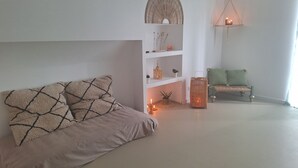 Uma sala de estar minimalista com um sofá, uma mesinha com velas, um lustre pendente e um banco verde.