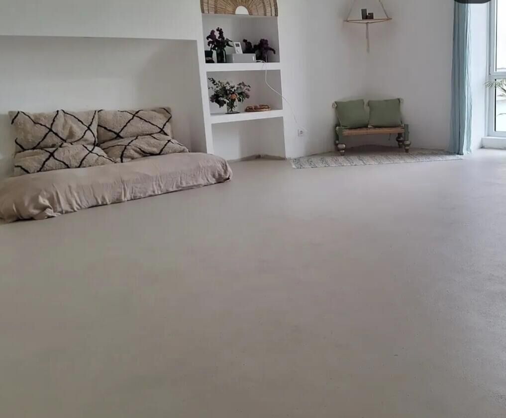 Ein geräumiger Raum mit großem Fenster, einer Couch, einer Bank und einer weißen Regaleinheit mit Dekorationselementen.