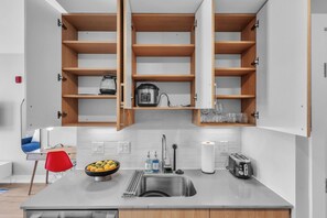 A modern kitchen with a stainless steel sink, a bowl of fruit, a toaster, and wooden cabinets.