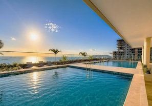 Ein Schwimmbad mit Liegestühlen, Blick aufs Meer und ein Gebäude mit Balkon.