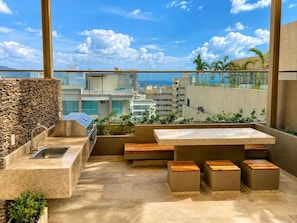 Eine Dachterrasse mit einer Steinmauer, einem Grill, einer Spüle und Holzmöbeln.