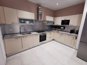 A modern kitchen with beige cabinetry, a stainless steel range hood, a built-in microwave, and a dishwasher.