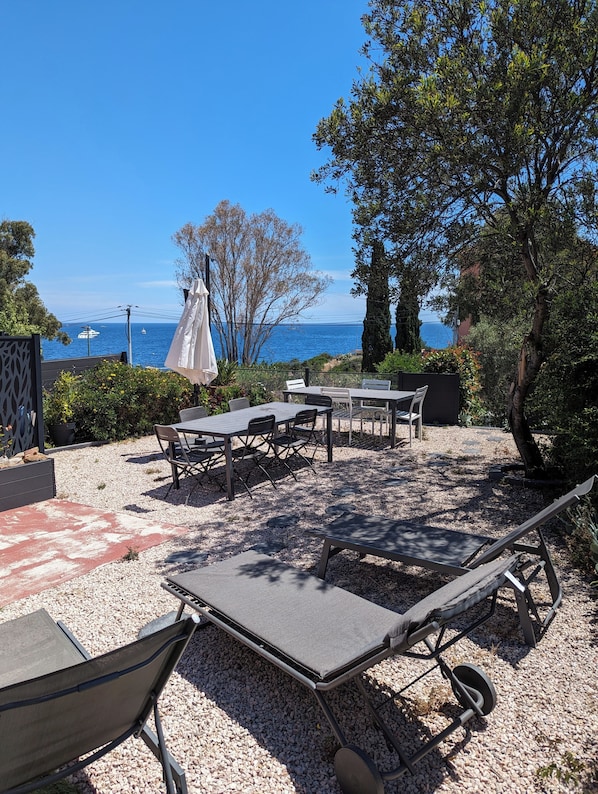 An outdoor seating area with tables and chairs, a hammock, and a view of the sea.