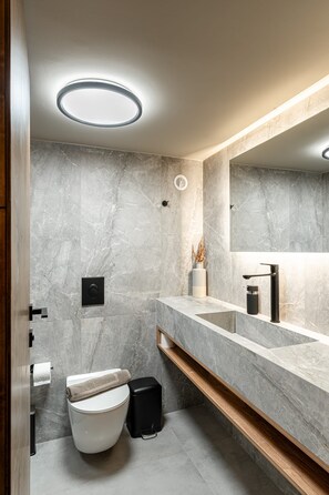 Et moderne badeværelse med en marmorvæg, et stort spejl, et toilet og en vask med en træhylde.