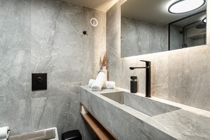 Ein modernes Badezimmer mit Marmorwand, Waschbecken, Spiegel und Handtuchhalter.