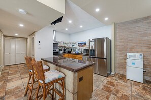 A kitchen with a central island, wooden chairs, a refrigerator, and a microwave. - Vacation Mode Starts Here — Pool, Pier and Great Views (Port Aransas)