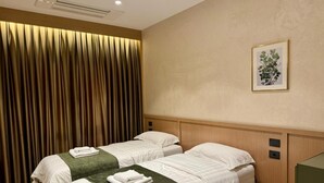 Quarto de hotel com duas camas, uma janela grande com cortinas, um quadro emoldurado na parede e cabeceira de madeira.