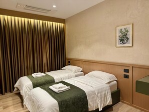Camera d'albergo con due letti, un'ampia finestra con tende, un quadro incorniciato al muro e una testiera in legno.