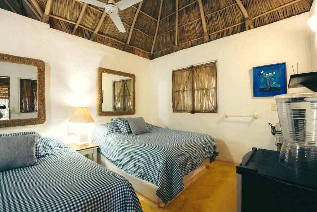 A room with two beds, a ceiling fan, a water dispenser, and a painting on the wall.