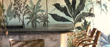 Una habitación con un mural de follaje tropical, muebles de mimbre y un techo de paja.