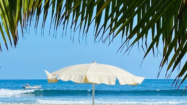 Una playa con dos sillas de playa y una sombrilla grande, con vista al océano.