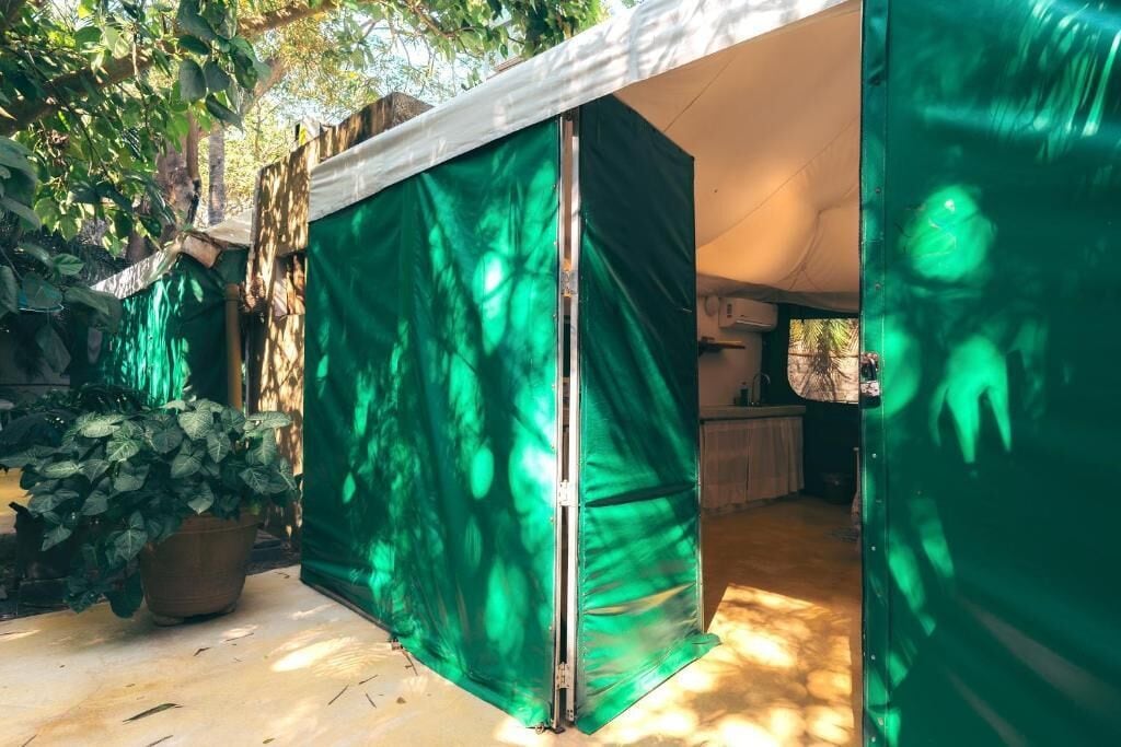 A tent with a door, a potted plant, and a kitchen area visible inside.