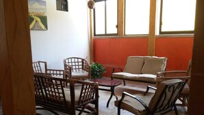 Una habitación con suelo de baldosas, un sofá, dos sillones, una mesita y una planta en maceta.