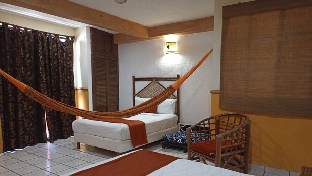Una habitación con dos camas, una hamaca, una silla de madera y una ventana con cortinas.