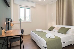 Ein Hotelzimmer mit Bett, Schreibtisch mit Stuhl, Fenster und Wandlampe.