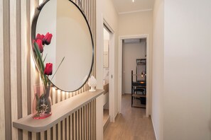 Un couloir avec un miroir, un vase rempli de fleurs rouges et une lampe.