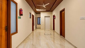 Un couloir avec des portes en bois, un ventilateur de plafond, un extincteur et un sol en marbre.