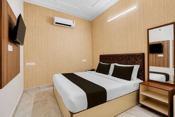 A hotel room with a bed, a bedside table, a mirror, and an air conditioning unit.